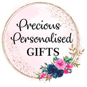 May include: A logo featuring the text "Precious Personalised GIFTS" in a black script font, set within a gold-lined circle with a pink watercolor background. A floral arrangement of pink and blue flowers adorns the bottom right.