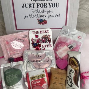 May include: A gift box filled with self-care items. Includes a lip mask, eye masks, a tea bag, a candle, a bar of chocolate, and a soap. The box also contains a decorative sign that reads "The Best Teacher Ever".