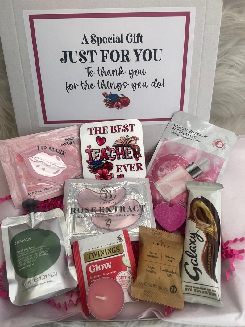 May include: A gift box filled with self-care items. Includes a lip mask, eye masks, a tea bag, a candle, a bar of chocolate, and a soap. The box also contains a decorative sign that reads "The Best Teacher Ever".