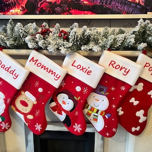 Pode incluir: Cinco meias de Natal vermelhas com punhos brancos, cada uma personalizada com nomes bordados: Daddy, Mommy, Loxie, Rory e Poppy. As meias apresentam personagens aplicados, incluindo o Pai Natal, uma rena, um pinguim e um boneco de neve.