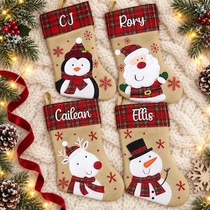 May include: Four tan Christmas stockings with red and green plaid cuffs. Each cuff features a white embroidered name: CJ, Rory, Cailean, and Ellis. The stockings display felt appliques of a penguin, Santa Claus, a reindeer, and a snowman.