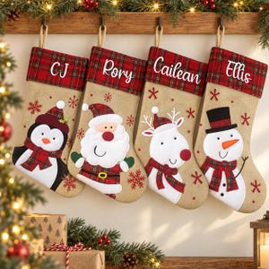 May include: Four hessian Christmas stockings with red tartan cuffs, each personalised with names CJ, Rory, Cailean, and Ellis. The stockings feature appliqued characters including a penguin, Santa Claus, a reindeer, and a snowman with red snowflake accents.