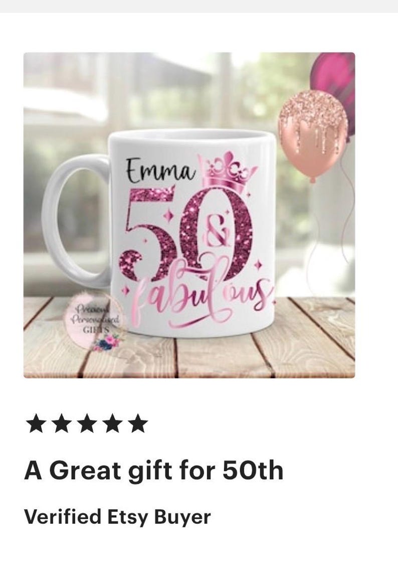 May include: White ceramic mug with a handle, featuring the name "Emma" above a large "50" and the word "fabulous" in pink script. The design includes a crown and glitter accents. A pink balloon is visible in the background.