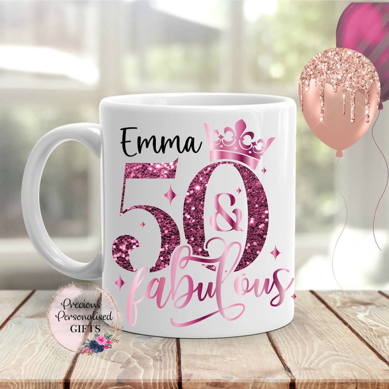 May include: White ceramic mug with the name "Emma" and the text "50 & fabulous" in pink glitter lettering. A pink crown and star accents decorate the mug. A "Precious Personalised GIFTS" logo is visible.