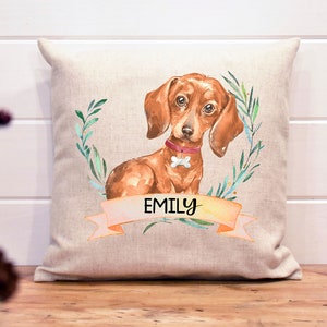 May include: A beige linen pillow with a watercolor illustration of a dachshund dog with a pink collar and the name "Emily" on a banner.
