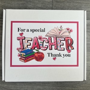May include: White gift box with a pink border featuring the text "For a special TEACHER Thank you." The word TEACHER is in a colorful, patterned font, with an open book, apple, and books graphic.