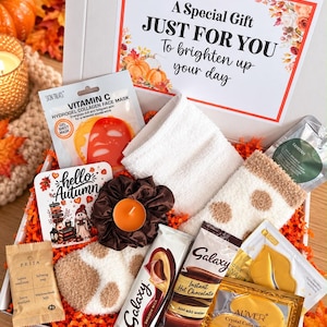 May include: A gift box containing a Vitamin C hydrogel face mask, a white washcloth, fuzzy socks with brown spots, a brown scrunchie, an orange tea light candle, a Galaxy chocolate bar, hot chocolate mix, gold lip and eye masks, and Prija soap.