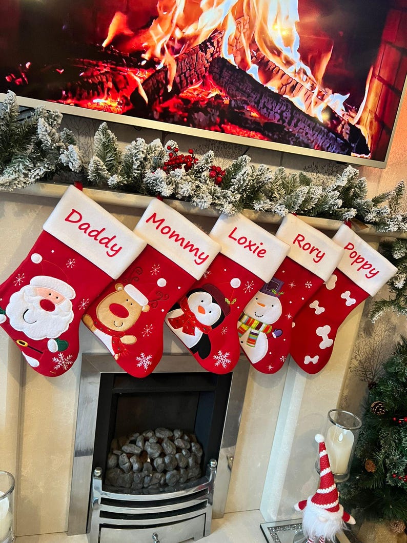 Pode incluir: Cinco meias de Natal vermelhas com punhos brancos, cada uma personalizada com nomes bordados: Daddy, Mommy, Loxie, Rory e Poppy. As meias apresentam aplica&ccedil;&otilde;es festivas, incluindo o Pai Natal, uma rena, um pinguim, um boneco de neve e padr&otilde;es de ossos brancos.