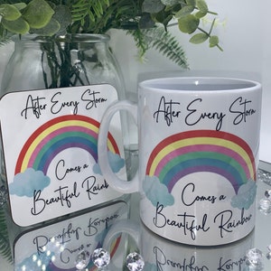 May include: White ceramic mug and coaster set with a rainbow and clouds design. The mug and coaster both feature the text "After Every Storm Comes a Beautiful Rainbow".