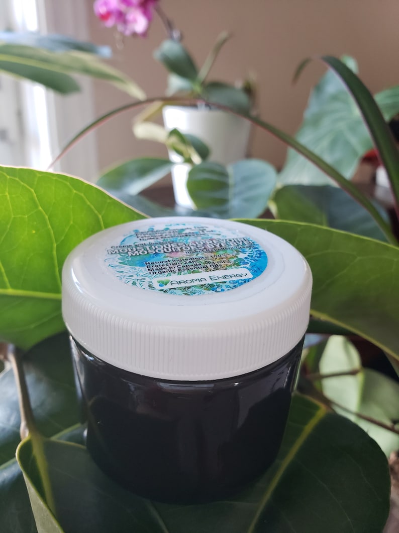 Może przedstawiać: Mały, biały słoik z czarną pokrywką, zawierający ciemny płyn. Etykieta na słoiku głosi "Natural Repellent Mosquito Oil" z napisami "Made with Essential Oils" i "Aroma Energy" poniżej.