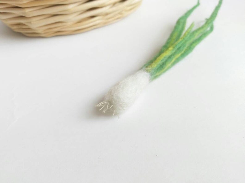 May include: A hand-felted green onion with a white bulb and green leaves. The onion is made of wool and is a realistic representation of a real onion.