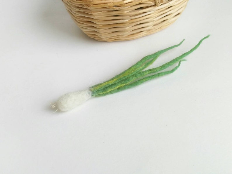 May include: A hand-felted green onion with a white bulb. The onion is made of wool and has a realistic appearance.