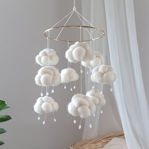 May include: A white felt cloud mobile with crystal raindrops hanging from each cloud. The mobile is suspended from a gold metal ring.