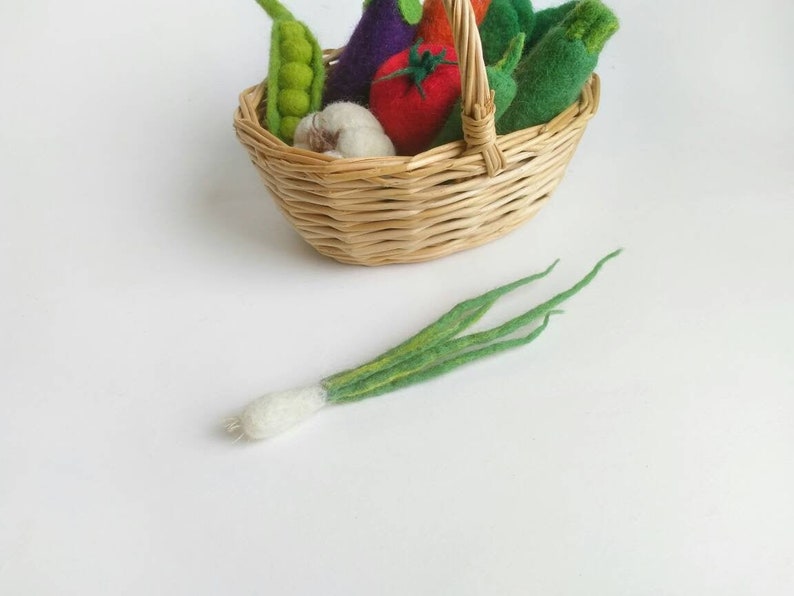 May include: A wicker basket filled with felt vegetables, including a green zucchini, a purple eggplant, a red tomato, a green pea pod, a white garlic, and a green onion.