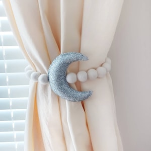 May include: A silver glitter crescent moon curtain tieback with a white pom pom trim.