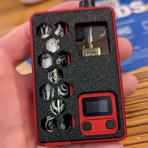 May include: A red and black electronic vaping device with a digital display and two buttons. The device has a clear window showing a gold atomizer. The device has a black and white patterned design.