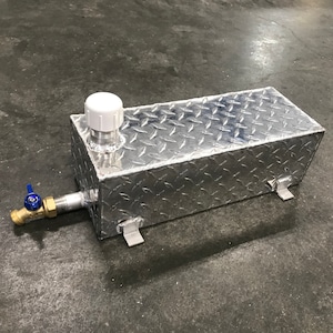 May include: A silver metal rectangular tank with a diamond plate pattern. The tank has a white plastic cap on top and a brass valve with a blue handle on the side.