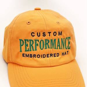 May include: Orange baseball cap with black and green embroidery that reads "CUSTOM PERFORMANCE EMBROIDERED HAT"