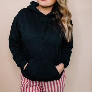 May include: A black hooded sweatshirt with a kangaroo pocket. The sweatshirt is worn over red and white striped pants.