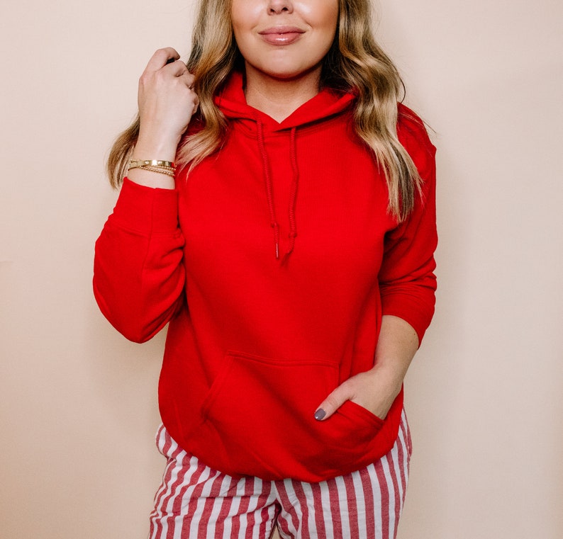 May include: A red hooded sweatshirt with a kangaroo pocket. The sweatshirt is worn by a person with long blonde hair and is paired with red and white striped pants.