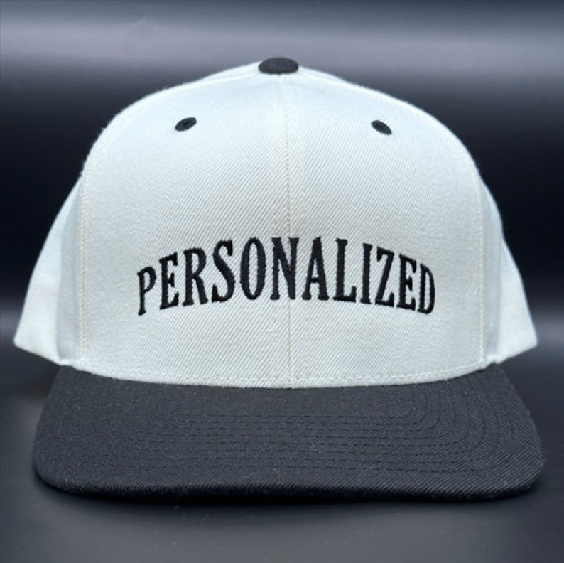 Może przedstawiać: Biało-czarna czapka z daszkiem z wyhaftowanym na przodzie napisem "PERSONALIZED" w kolorze czarnym.