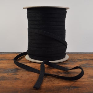 May include: A spool of black elastic trim, wound on a cardboard spool. The elastic is about 1/2 inch wide and has a ribbed texture.