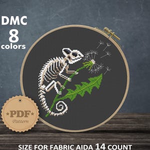 Könnte beinhalten: Ein Kreuzstichmuster mit einem Chamäleon-Skelett auf einem Löwenzahn, in einem hölzernen Stickrahmen. Das Design verwendet 8 Farben und ist für 14-Count-Aida-Stoff. Das fertige Stück misst 14,88 x 15,97 cm. Das Muster ist ein PDF.