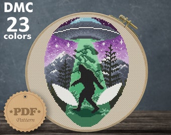May include: Cross stitch pattern featuring a green alien with a UFO in the background. The alien is standing in a forest with mountains and stars. The pattern is for Aida 14 count fabric and measures 6.14 x 8.14 inches or 15.60 x 20.68 cm.