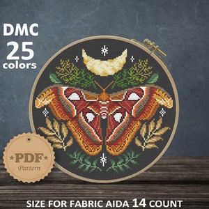 Op de afbeelding: Een kruissteekpatroon met een mot met een halve maan en bladeren. Het patroon is in een ronde hoepel en is 8,14 inch bij 7,71 inch. Het patroon vereist 25 kleuren DMC-garen en is voor Aida 14 count stof.