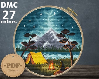 May include: A cross stitch pattern of a camping scene with a tent, campfire, and mountains under a starry night sky. The pattern is in a wooden embroidery hoop and is 8.21 inches by 8.14 inches. The pattern requires 27 DMC colors and is for Aida 14 count fabric.