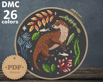 May include: A cross-stitch pattern featuring a brown otter with a dark gray background. The otter is surrounded by green leaves, red and orange flowers, and small blue fish. The pattern is in a round embroidery hoop and is labeled "DMC 26 colors" and "PDF Pattern". The size of the pattern is 19.59 x 20.32 cm or 108 x 112 stitches, which is 7.71 x 8.00 inches.
