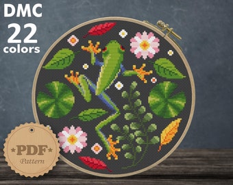 May include: A cross-stitch pattern featuring a green tree frog on a black background with pink flowers, green leaves, and yellow and red accents. The pattern is for Aida 14 count fabric and measures 7.64 x 7.79 inches or 19.41 x 19.78 cm. The pattern requires 22 DMC colors.
