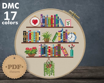 May include: A cross-stitch pattern featuring a bookshelf with books, plants, a clock, and a heart. The pattern is designed for 14 count Aida fabric and measures 6.79 x 7.43 inches or 17.24 x 18.87 cm. The pattern requires 17 DMC colors.