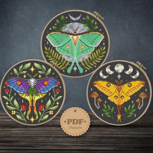 Puede incluir: Tres patrones de punto de cruz redondos con polillas en colores vibrantes. Una polilla es verde, otra amarilla y la tercera es una mezcla de morado, azul y amarillo. Cada diseño está sobre un fondo oscuro con elementos florales y celestiales.