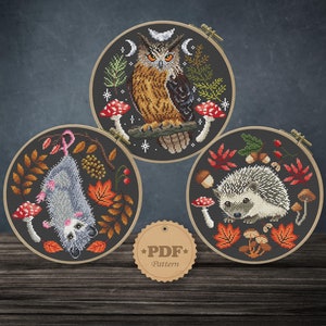 May include: Three embroidery patterns featuring a gray opossum, a brown owl, and a gray hedgehog. Each pattern is surrounded by a brown wooden hoop and features autumn leaves, mushrooms, and other forest elements. The text "PDF Pattern" is on a brown tag.