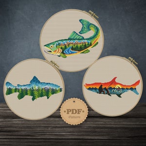 Puede incluir: Tres patrones de bordado en aro que representan peces coloridos con paisajes de montaña y bosque. Los aros están sobre una superficie de madera con una etiqueta "PDF Pattern".