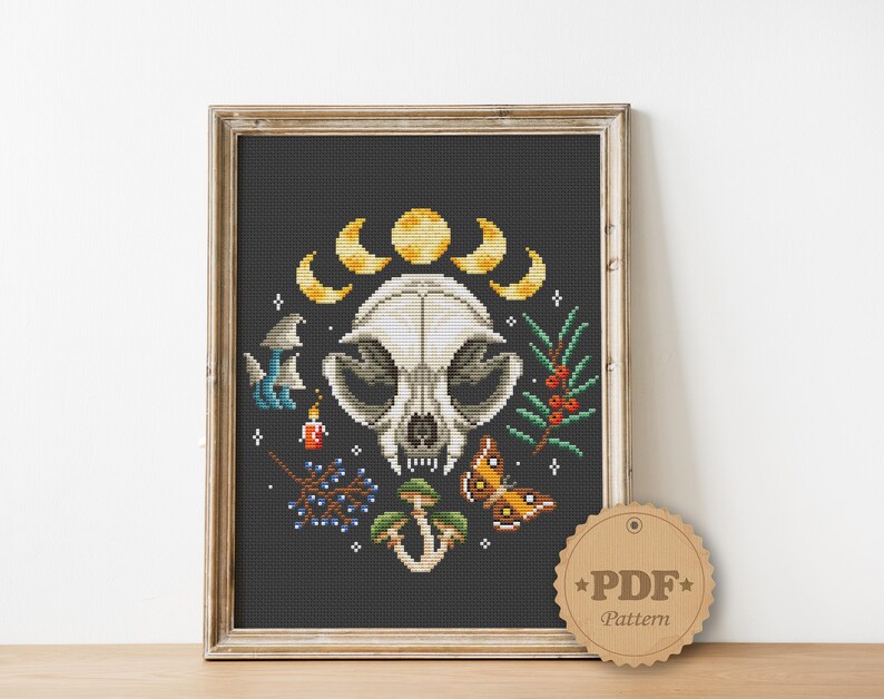 May include: Cross stitch pattern featuring a white animal skull with a crescent moon and stars, surrounded by mushrooms, berries, and a butterfly on a black background. The pattern is available as a PDF download.