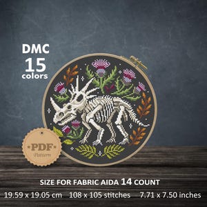 Può includere: Uno schema a punto croce in un telaio di legno con uno scheletro di dinosauro bianco circondato da fiori di cardo viola e foglie arancioni su sfondo nero. Il testo include DMC 15 colori, PDF Pattern e dimensioni 19,59 x 19,05 cm.