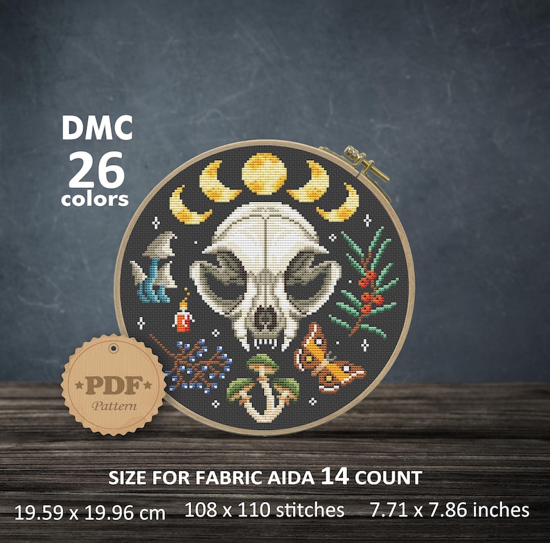 May include: A black and white cross stitch pattern of a cat skull with a crescent moon, mushrooms, berries, and butterflies. The pattern is in a round hoop and is 7.71 x 7.86 inches. The pattern requires 26 colors of DMC floss.