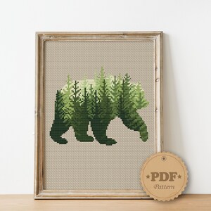 May include: Cross stitch pattern featuring a bear silhouette with a forest scene inside. The pattern is in a wooden frame and a brown tag with the text "PDF Pattern" is in the lower right corner.