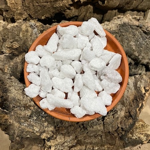 May include: A close-up of a small bowl filled with white incense chips. The bowl is made of terracotta and has a rough texture. The incense chips are irregularly shaped and have a slightly grainy texture.