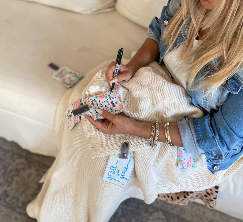 May include: A white blanket with floral patterned fabric tags attached. The tags have inspirational messages written on them, including "I'd pray for you, but I know you're already praying for me" and "you are grace".