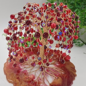 Könnte beinhalten: Eine rote und goldene Drahtbaumsculptur mit roten Glasperlen. Der Baum steht auf einem roten, weißen und goldenen Harzsockel.