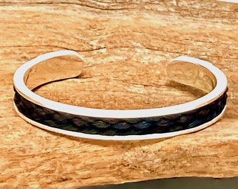 Puede incluir: Un brazalete de plata con una incrustación de cuero trenzado negro y azul.