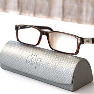 May include: Brown and clear eyeglasses with a silver accent on the temples and a matching silver case. The case has a textured surface and the word "döp" embossed on it. The eyeglasses are rectangular.