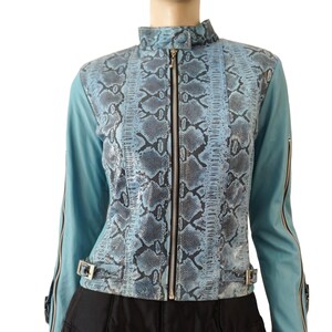 May include: A light blue jacket with a snakeskin pattern on the front and a high collar. The jacket has a zipper closure and silver hardware. The sleeves are solid light blue with zippers at the cuffs. The jacket is paired with a black skirt.