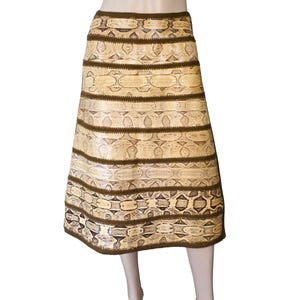 May include: A knee-length skirt with a snakeskin pattern in shades of beige and brown. The skirt features horizontal bands of the snakeskin pattern separated by dark brown trim. The skirt is displayed on a mannequin.