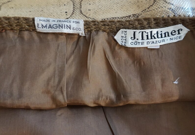 May include: Close-up of the interior of a garment, featuring two tags. One tag reads "MADE IN FRANCE FOR I. MAGNIN & CO." The other tag reads "J. Tiktiner C&Ocirc;TE D'AZUR - NICE". The lining is a light brown color.