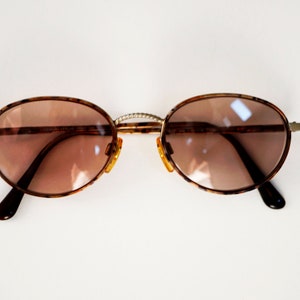 May include: A pair of oval-shaped sunglasses with brown tortoise shell frames and brown tinted lenses.