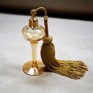 May include: A vintage amber glass perfume bottle with a gold metal atomizer and a gold tassel. The bottle has a round body and a long, slender neck.